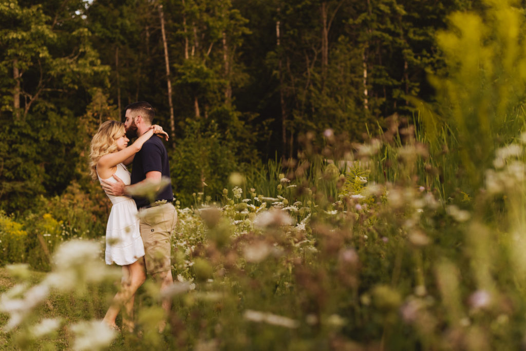engaged couple standing among wildflowers cuddling