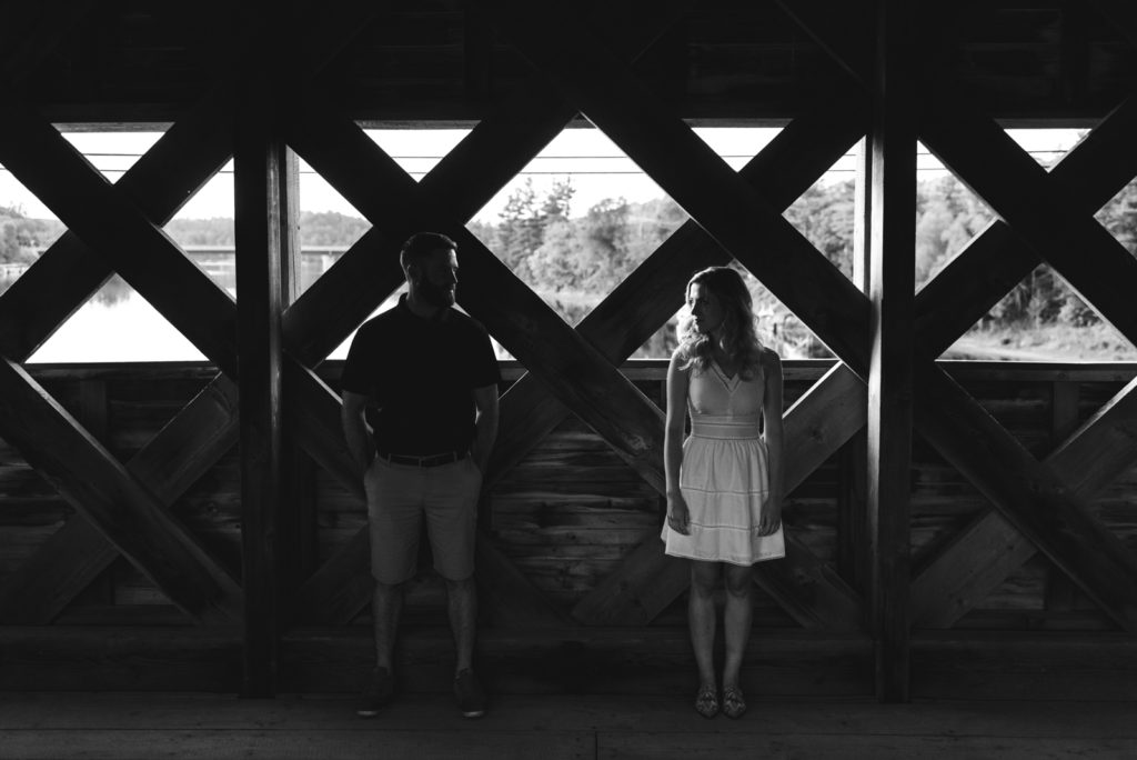 engaged couple standing on wakefield covered bridge in black and white silhouette
