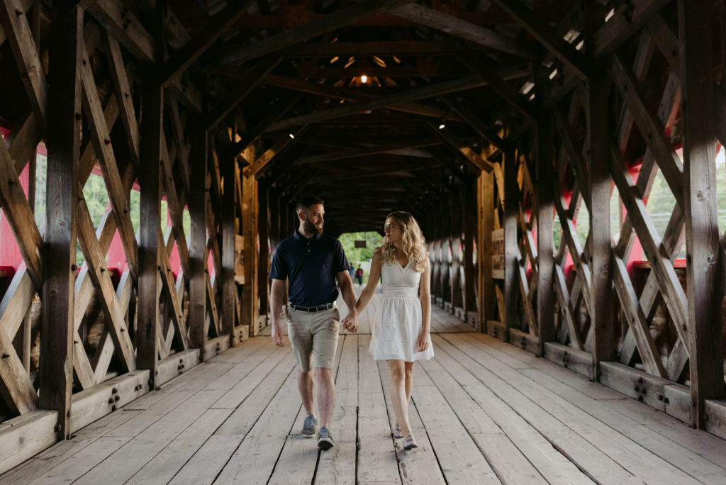 engaged couple holding hands walking along wakefield covered bridge