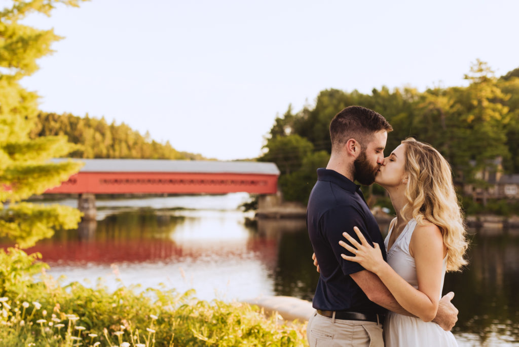 engaged couple kissing by the wakefield covered bridge at sunset