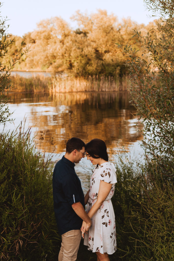 Engaged couple cuddling at sunset by the water