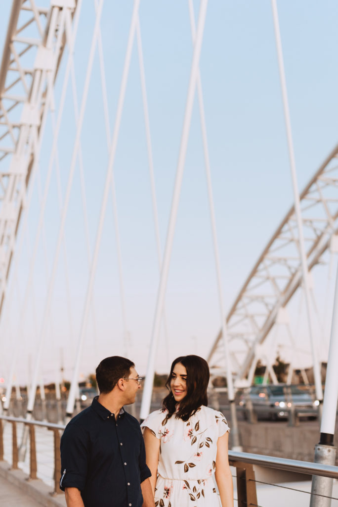 Engaged couple walking along big white bridge at sunset