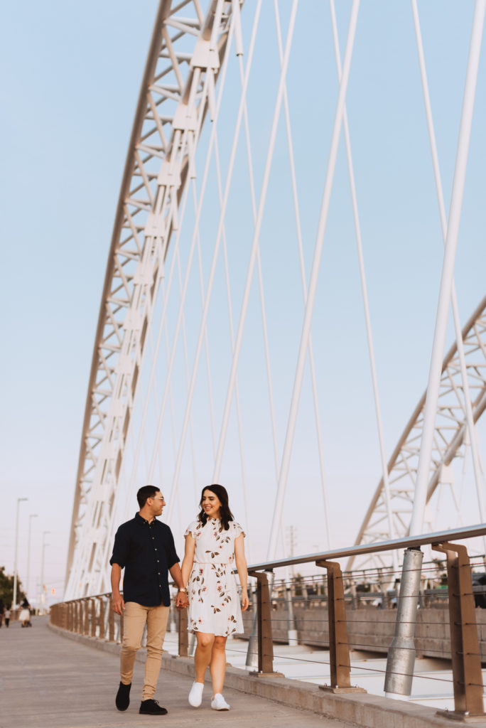 Engaged couple holding hands walking across big white bridge
