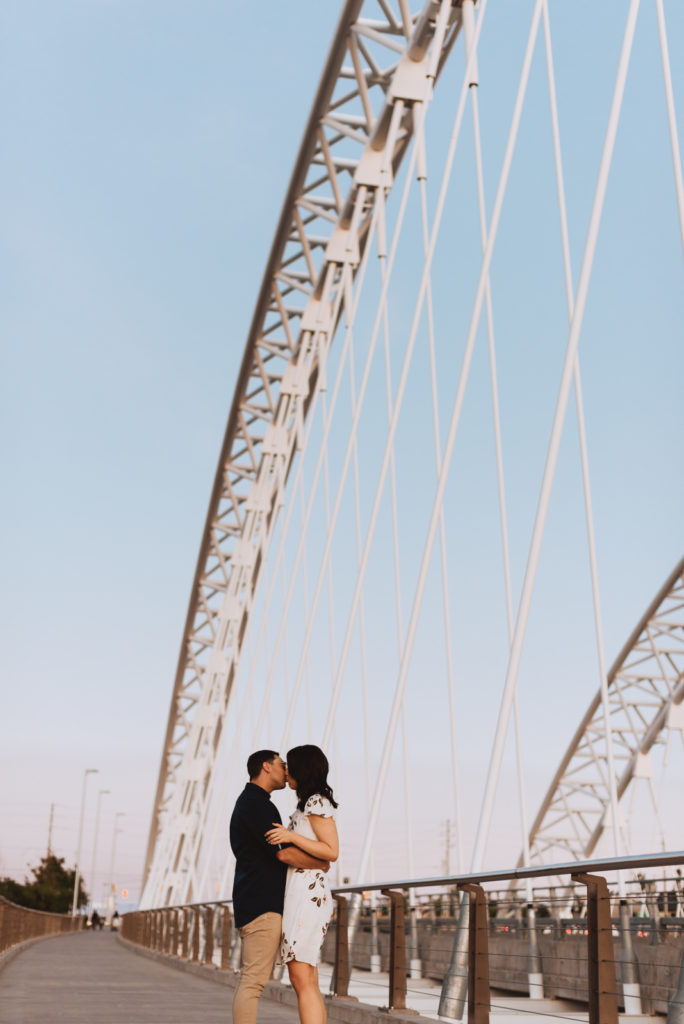 Engaged couple kissing on a big white bridge at sunset