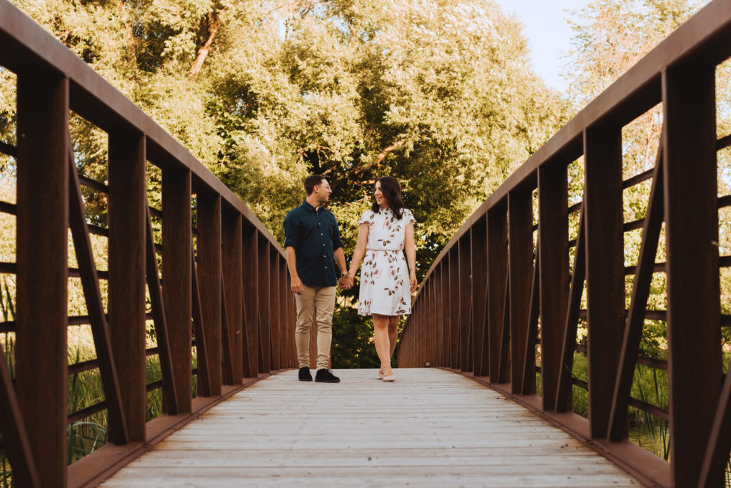 engaged couple holding hands walking along a bridge together