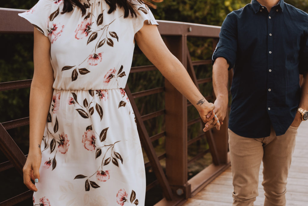 engaged couple holding hands walking along a bridge together