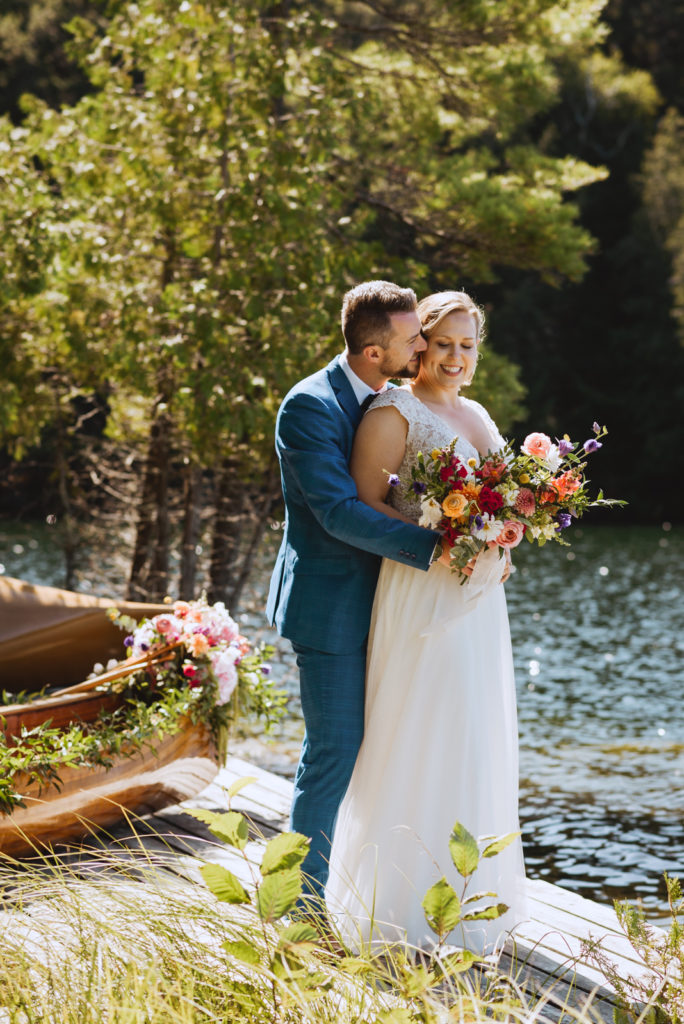 bride and groom on the dock cuddling with floral bouquet