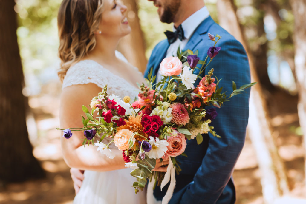 bride and groom in the forest with bright floral bouquet
