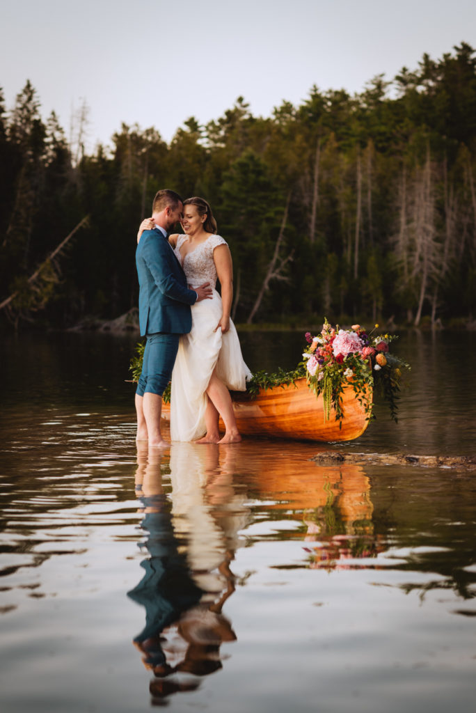 bride and groom standing in the water at sunset by floral canoe