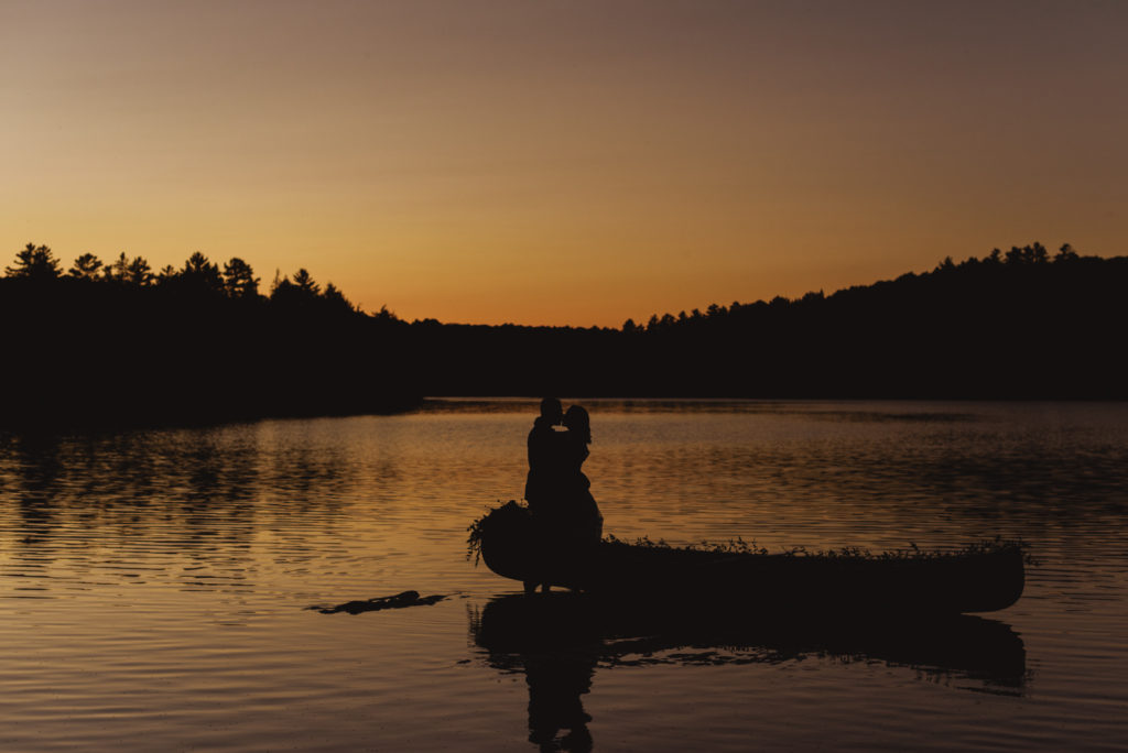 bride and groom silhouetted at sunset with a canoe in the water