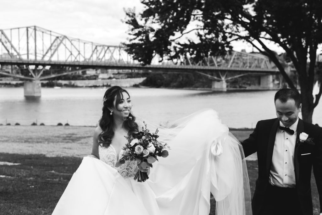 groom holding bride's train as they walk