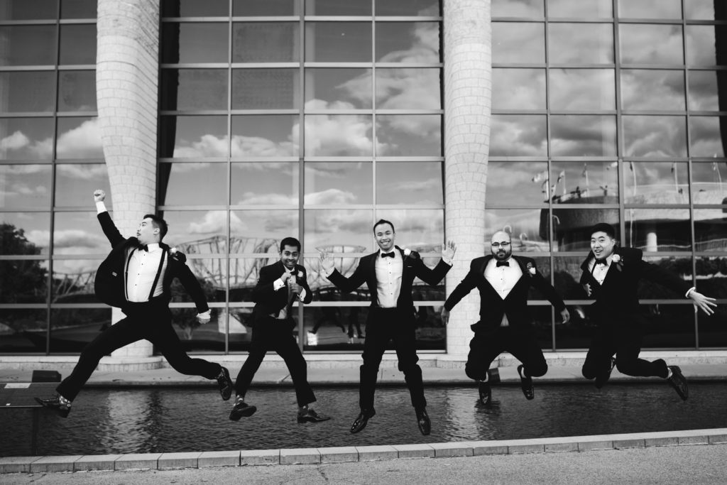 groom and groomsmen jumping in front of museum windows