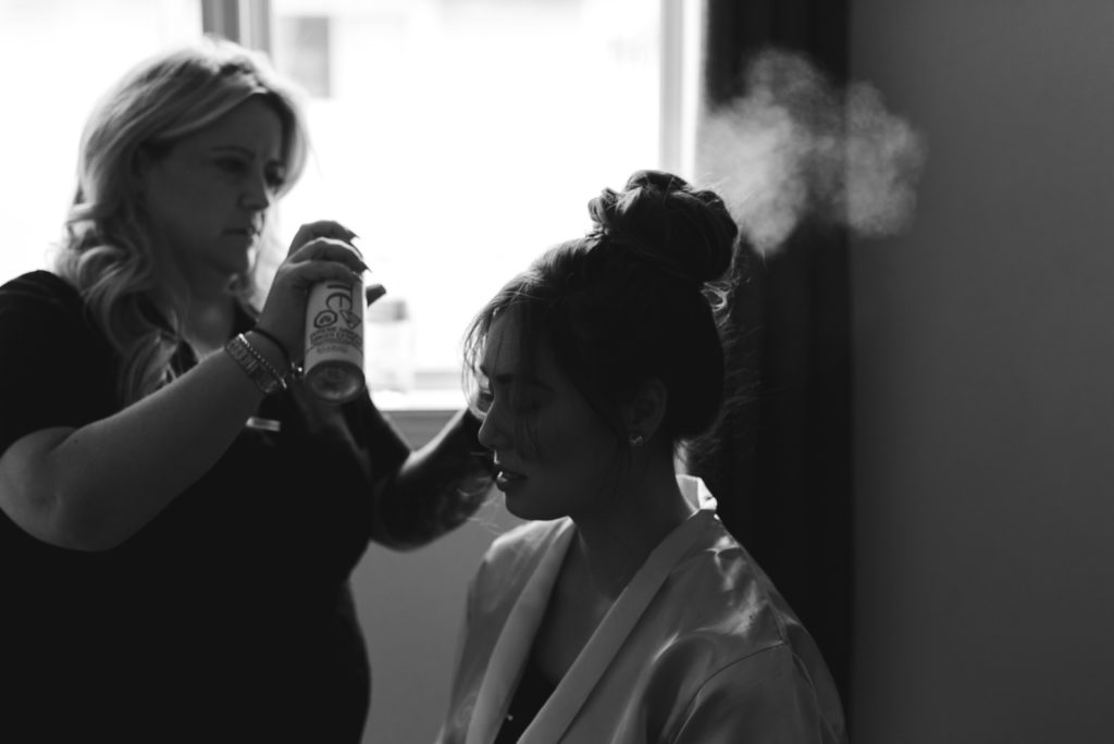 hair stylist spraying hair spray on bridesmaid's updo