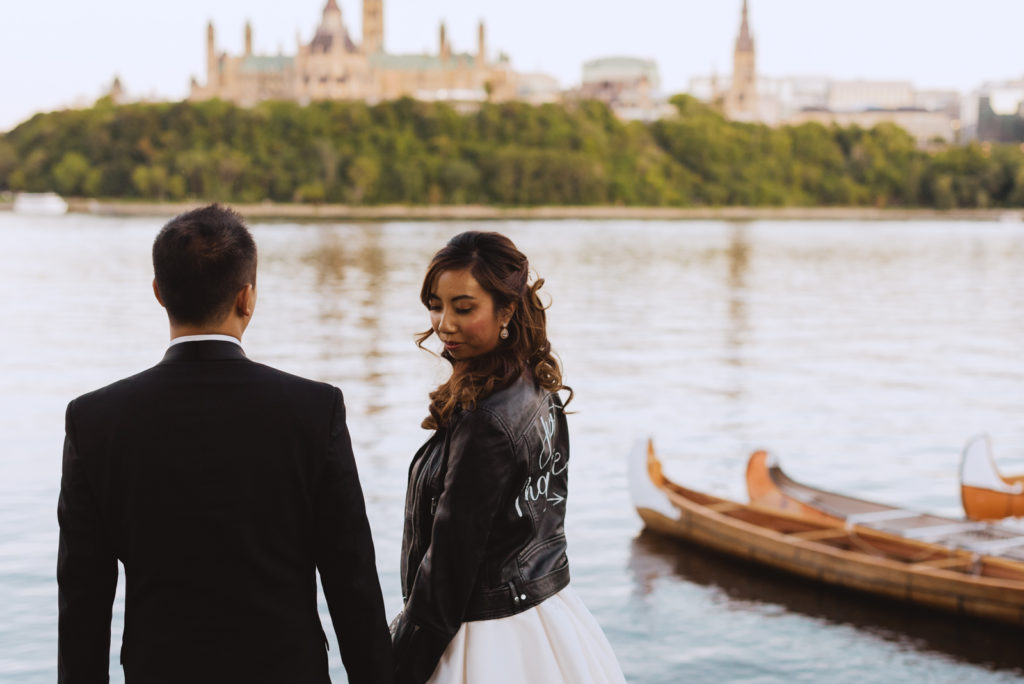 bride wearing the just married leather jacket by the water overlooking the parliament buildings at sunset