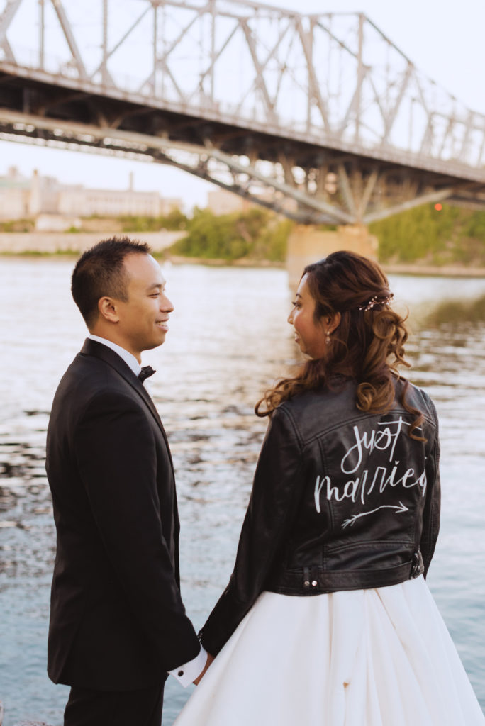 bride wearing the just married leather jacket by the water overlooking the river at sunset