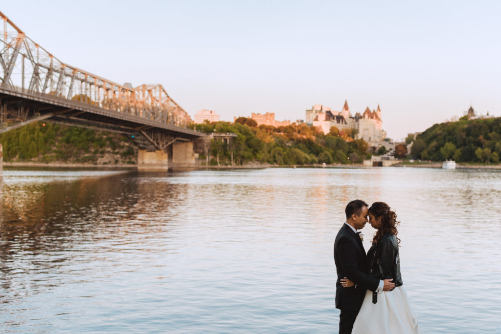 bride wearing just married leather jacket and groom at sunset by the water overlooking chateau laurier