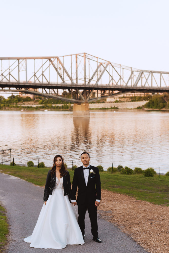 bride wearing just married leather jacket holding groom's hand overlooking alexandria bridge