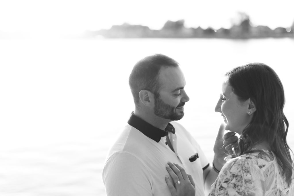 engaged couple laughing by the water at sunset in black and white