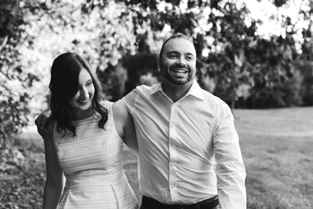 engaged couple with arms around each other walking and laughing in black and white