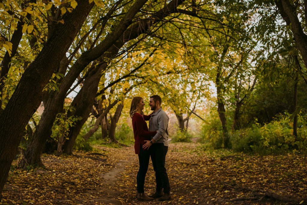 engaged couple underneath trees at sunset