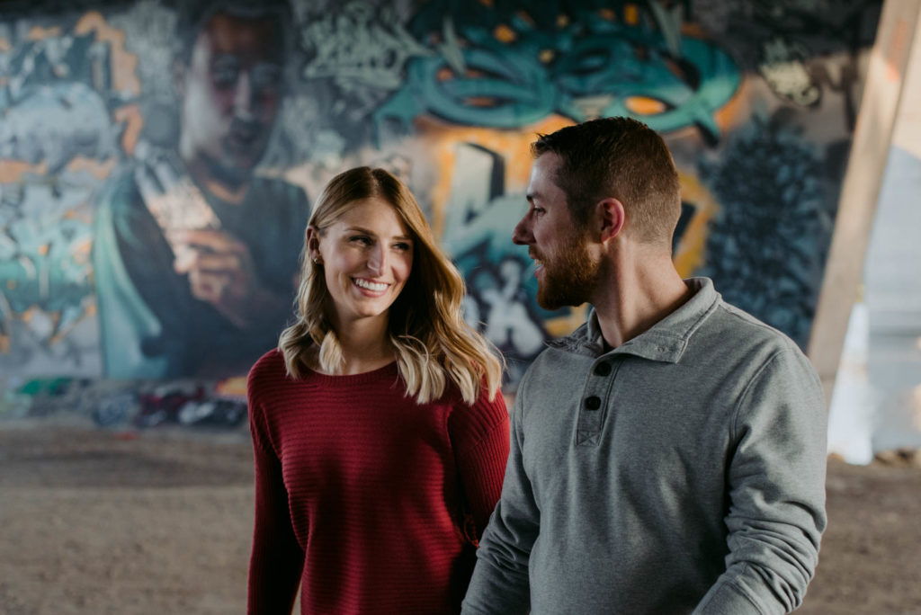 engaged couple walking together through graffiti wall house of paint