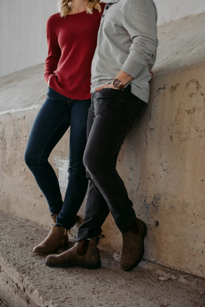 engaged couple leaning against a cement wall wearing blundstones