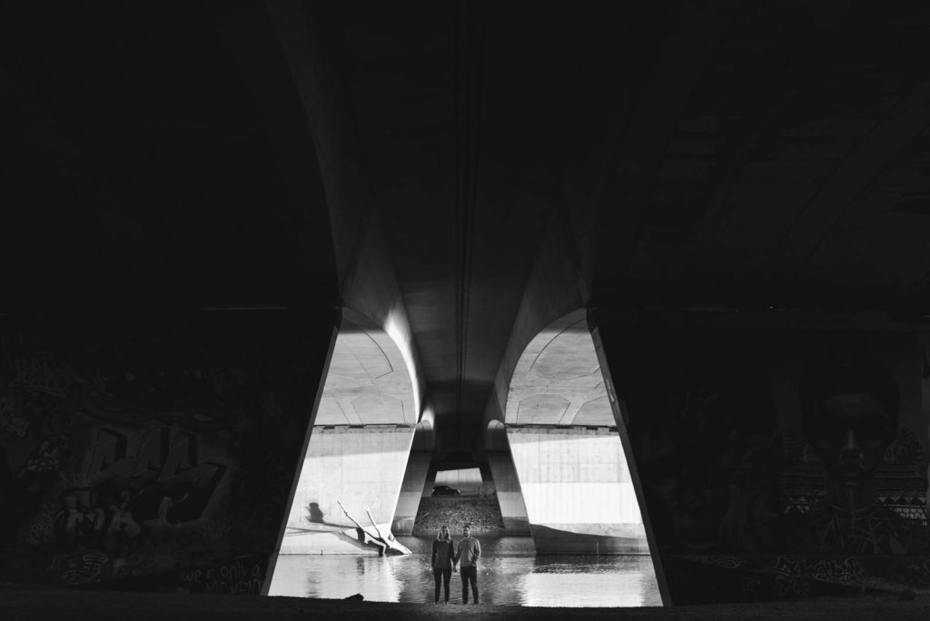 engaged couple standing under a bridge in black and white