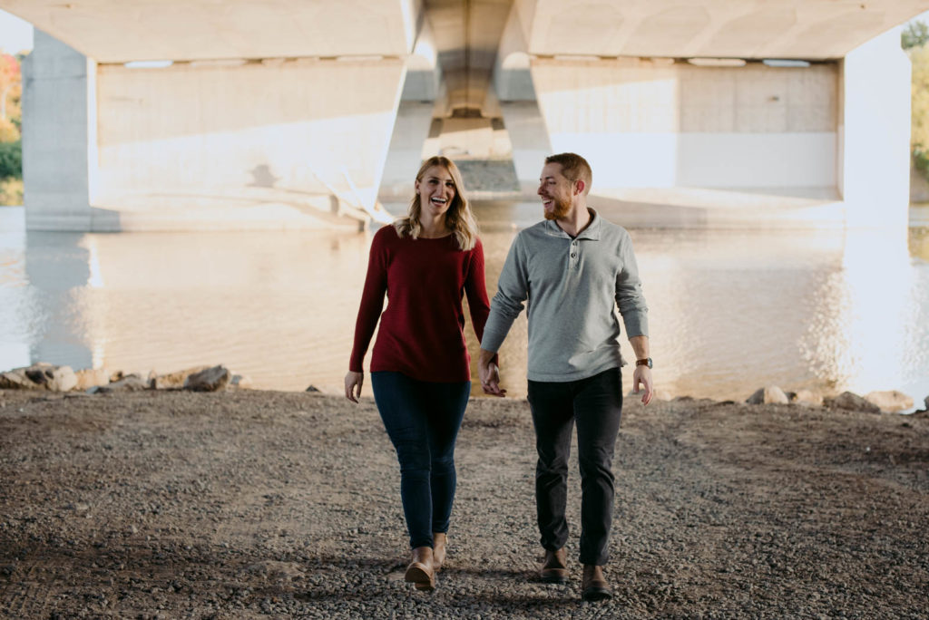 engaged couple walking under a bridge at sunset