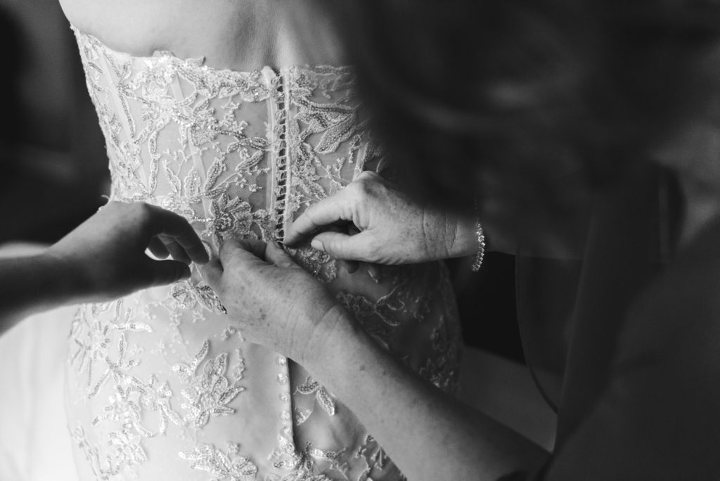mother of the bride tying up the bride's button on her dress
