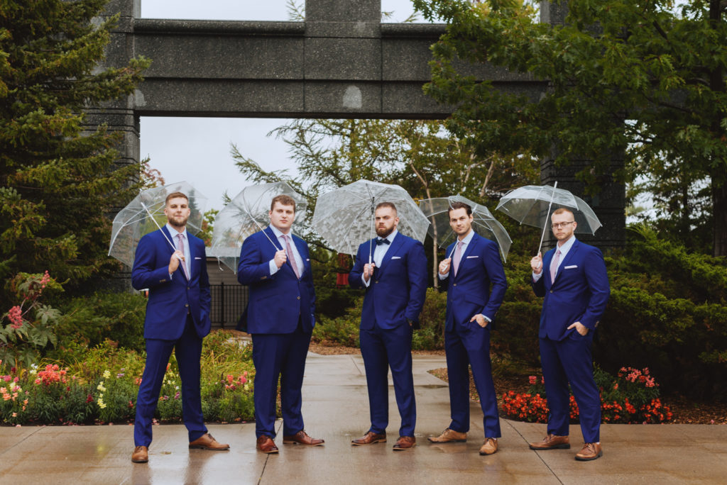 groom and groomsmen with umbrellas outside hotel