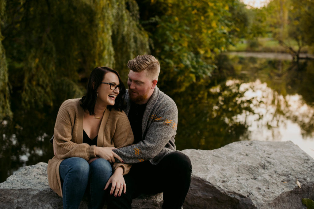 engaged couple laughing by a willow tree at sunset