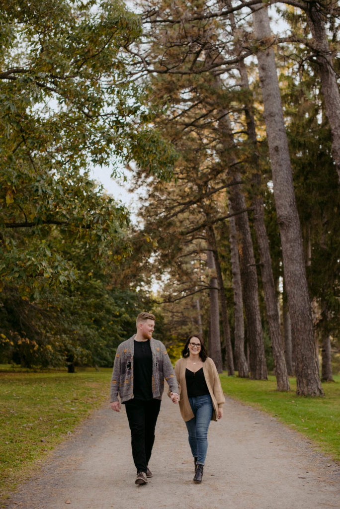 engaged couple holding hands and walking down a path in the woods