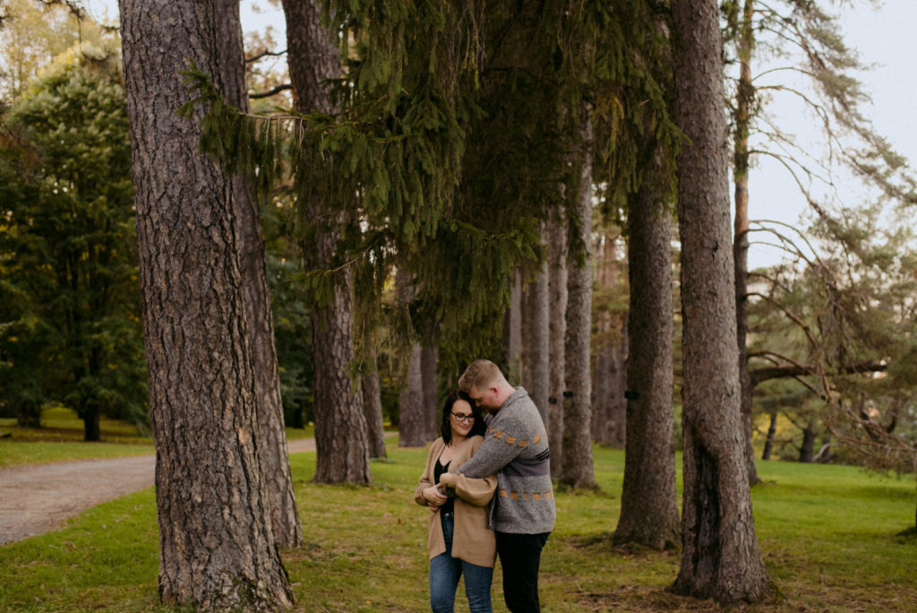 engaged couple cuddling among the trees in the woods