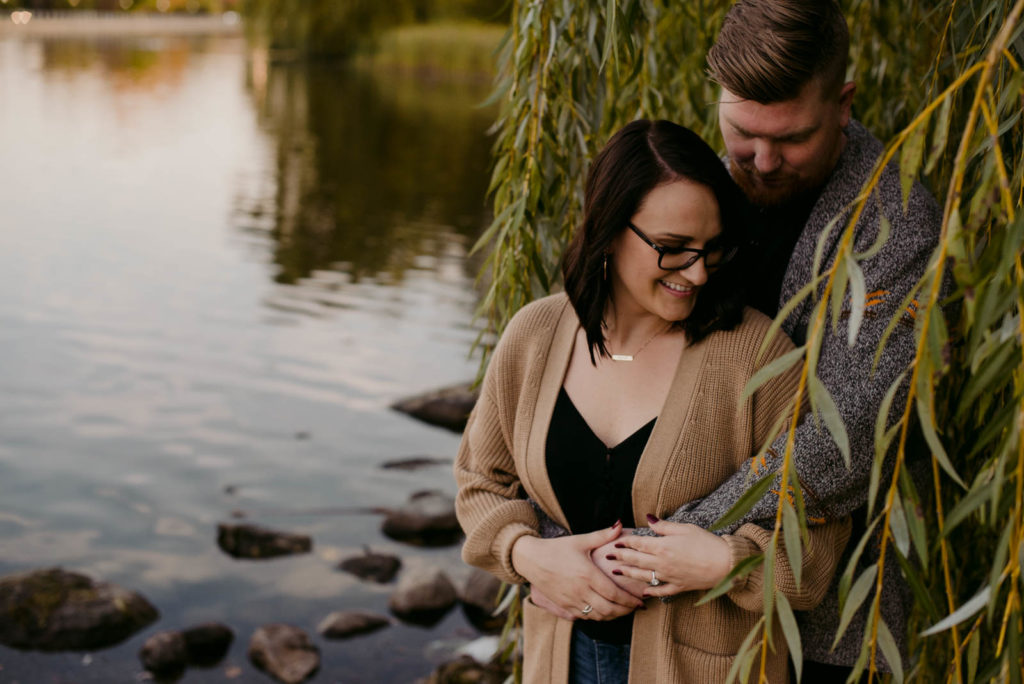 engaged couple by the water underneath a willow tree