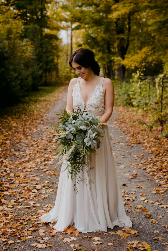 truvelle bride on dirt road with fall leaves holding wild green bouquet