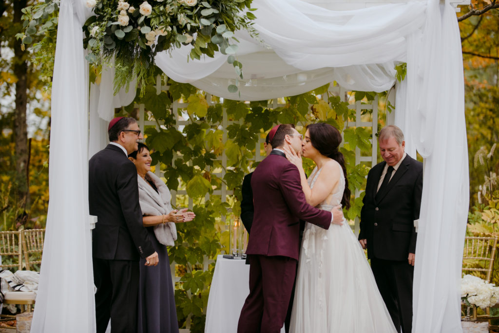 first kiss underneath chuppah during outdoor wedding ceremony