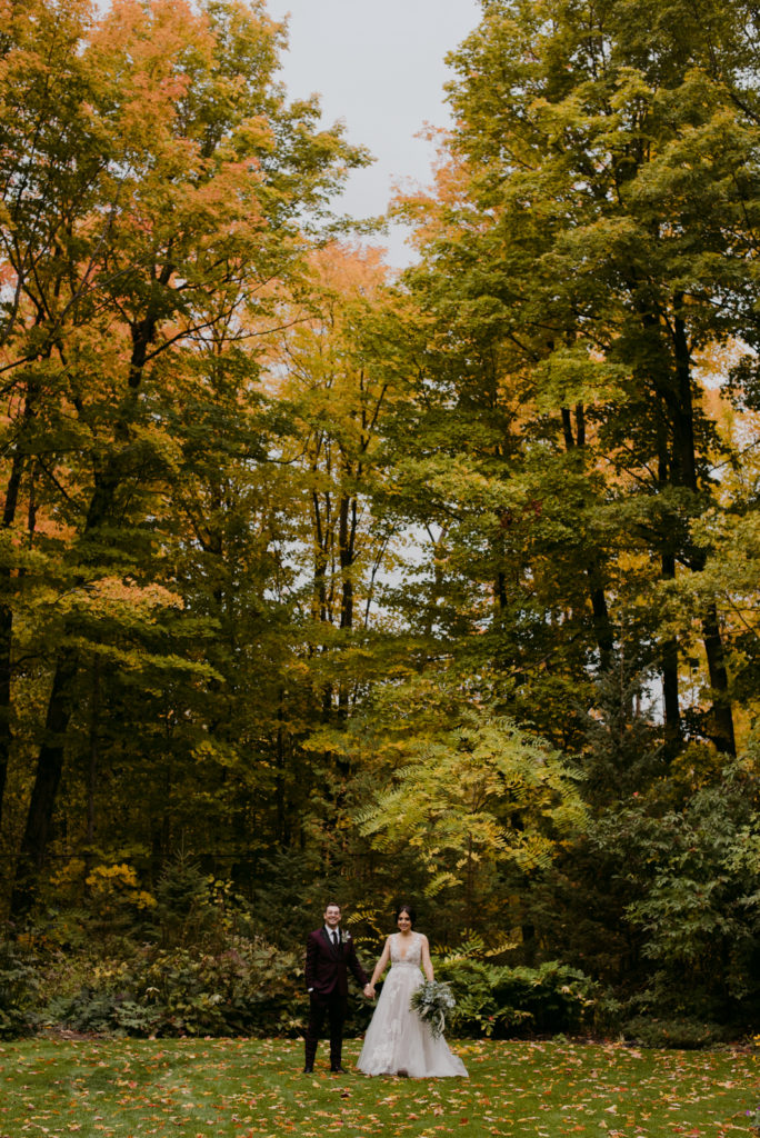 bride and groom holding hands among tall trees and fall leaves