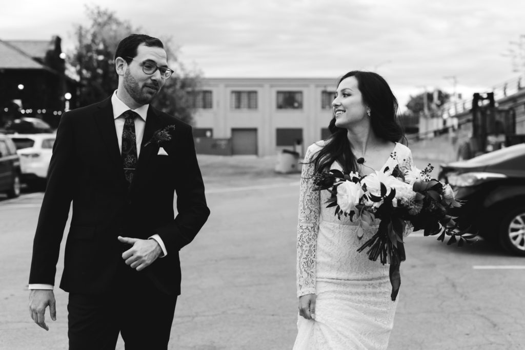 bride and groom walking across parking lot holding wild bouquet
