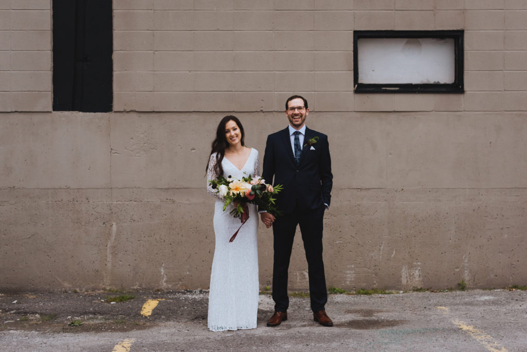 bride and groom holding hands against concrete wall in a parking lot