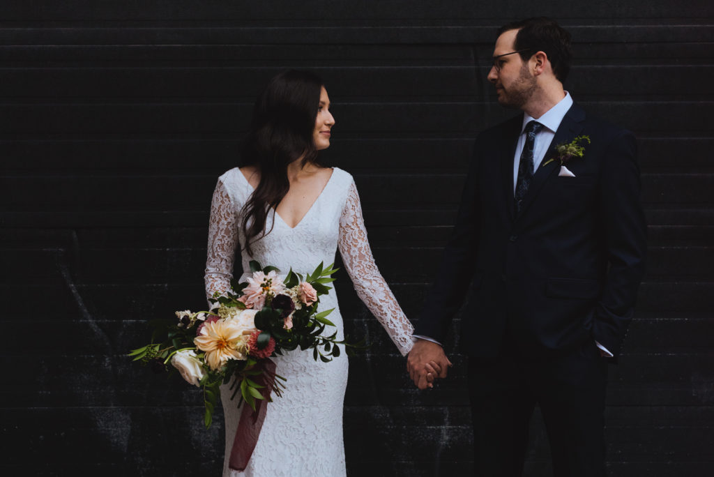 bride and groom holding hands against black garage door