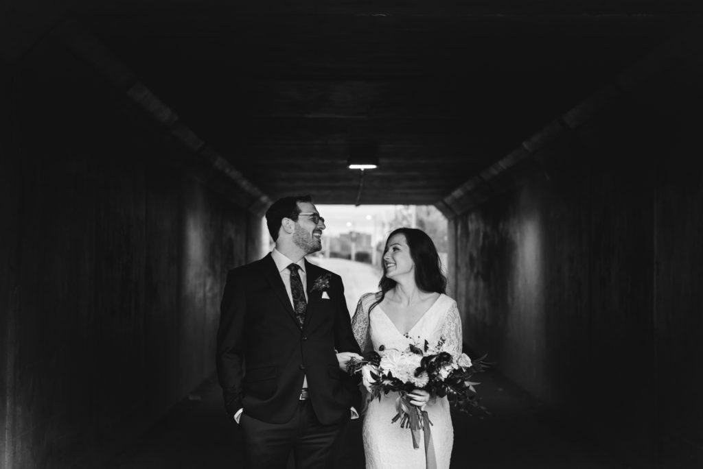 bride and groom laughing underneath a bridge in black and white