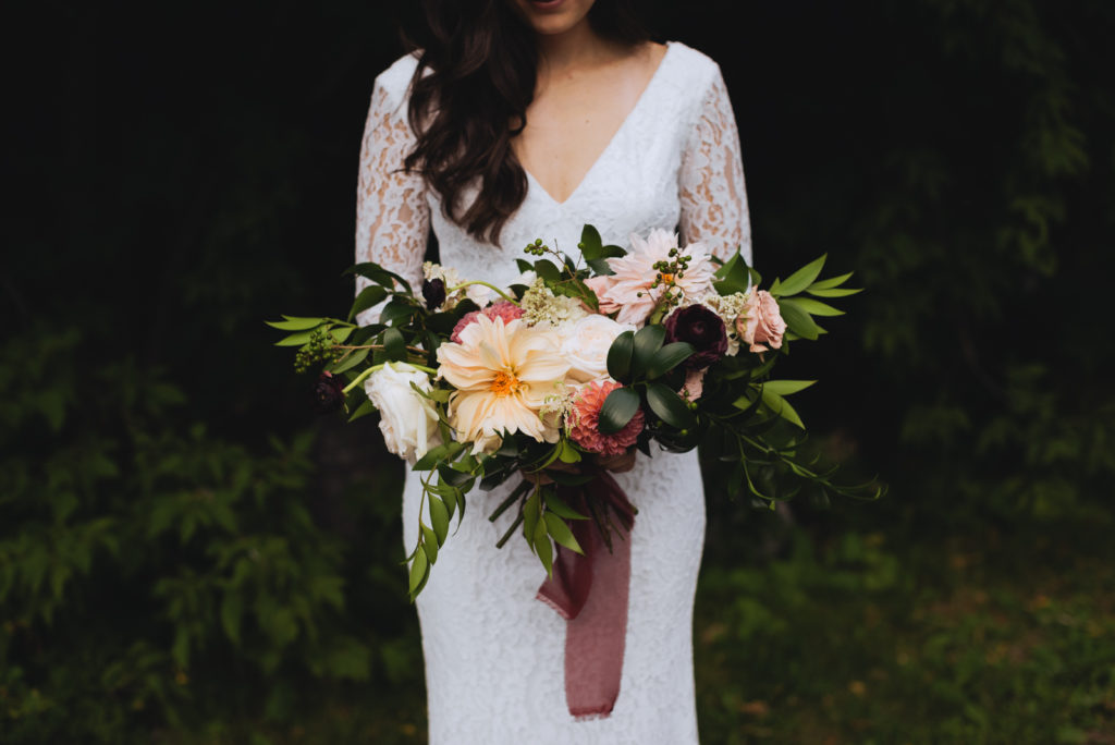 bride holding wild bouquet with trees in the background