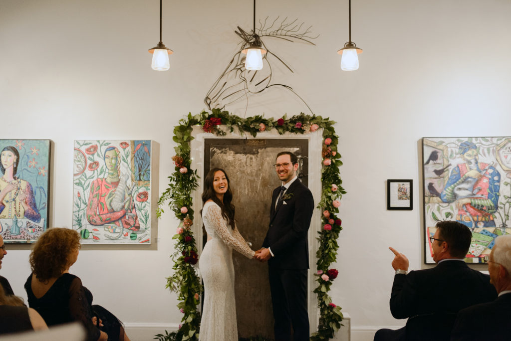 bride and groom laughing in front of metal door during orange art gallery wedding ceremony