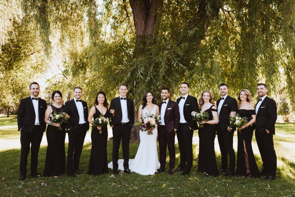 wedding party in black underneath a willow tree at sunset