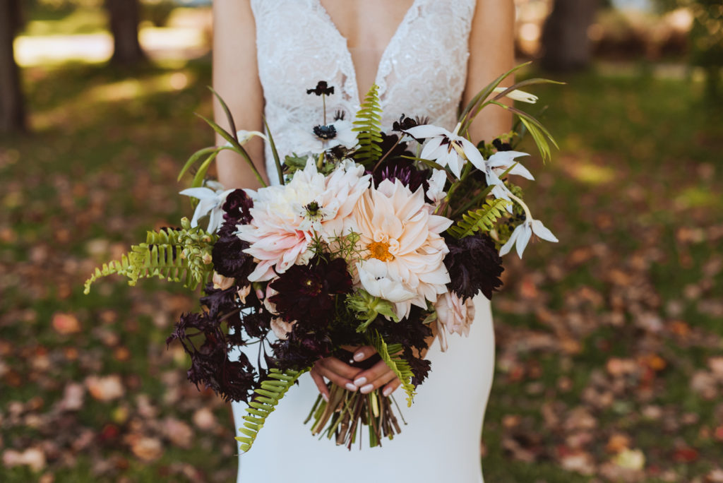 bride holding wild bouquet with ferns surrounded by fall leaves