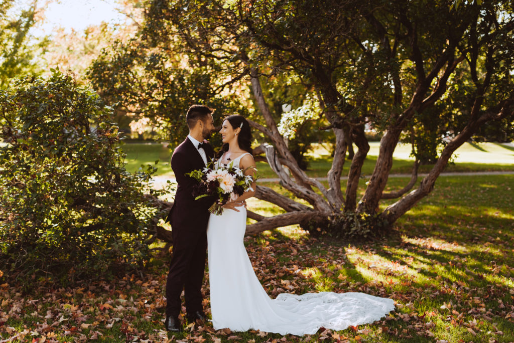 bride and groom underneath tree surrounded by fall leaves