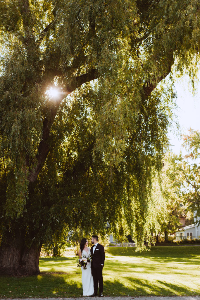 bride and groom underneath willow tree at sunset