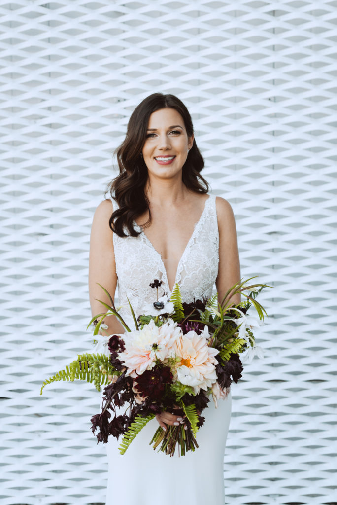 bride holding wild bouquet with ferns against white wall