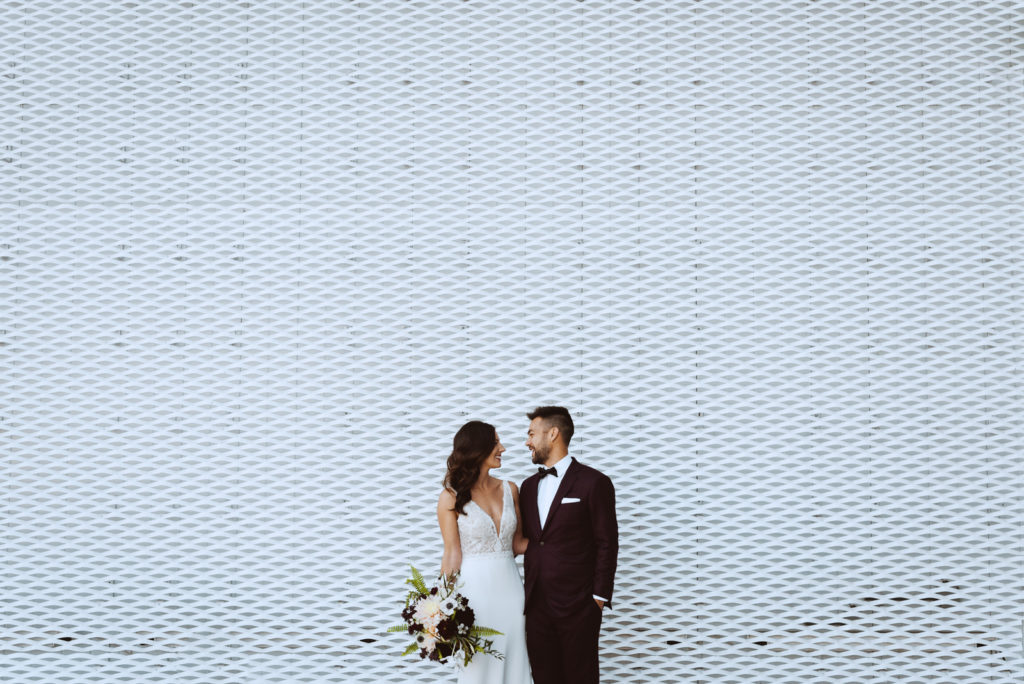 bride and groom in front of white metal wall