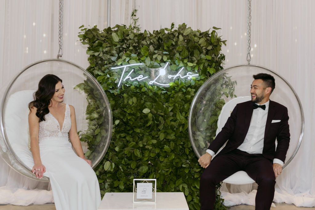 bride and groom sitting in bubble chairs with neon sign